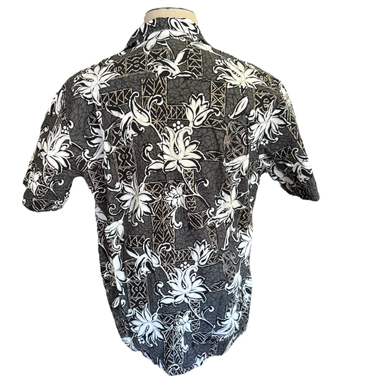 A short-sleeve button-up aloha shirt with a gray base and a white tropical floral ,displayed on a mannequin torso against a white background.