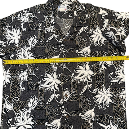 A gray aloha short-sleeve button-up shirt with a white floral , shown with a yellow tape measure across the chest to indicate width.