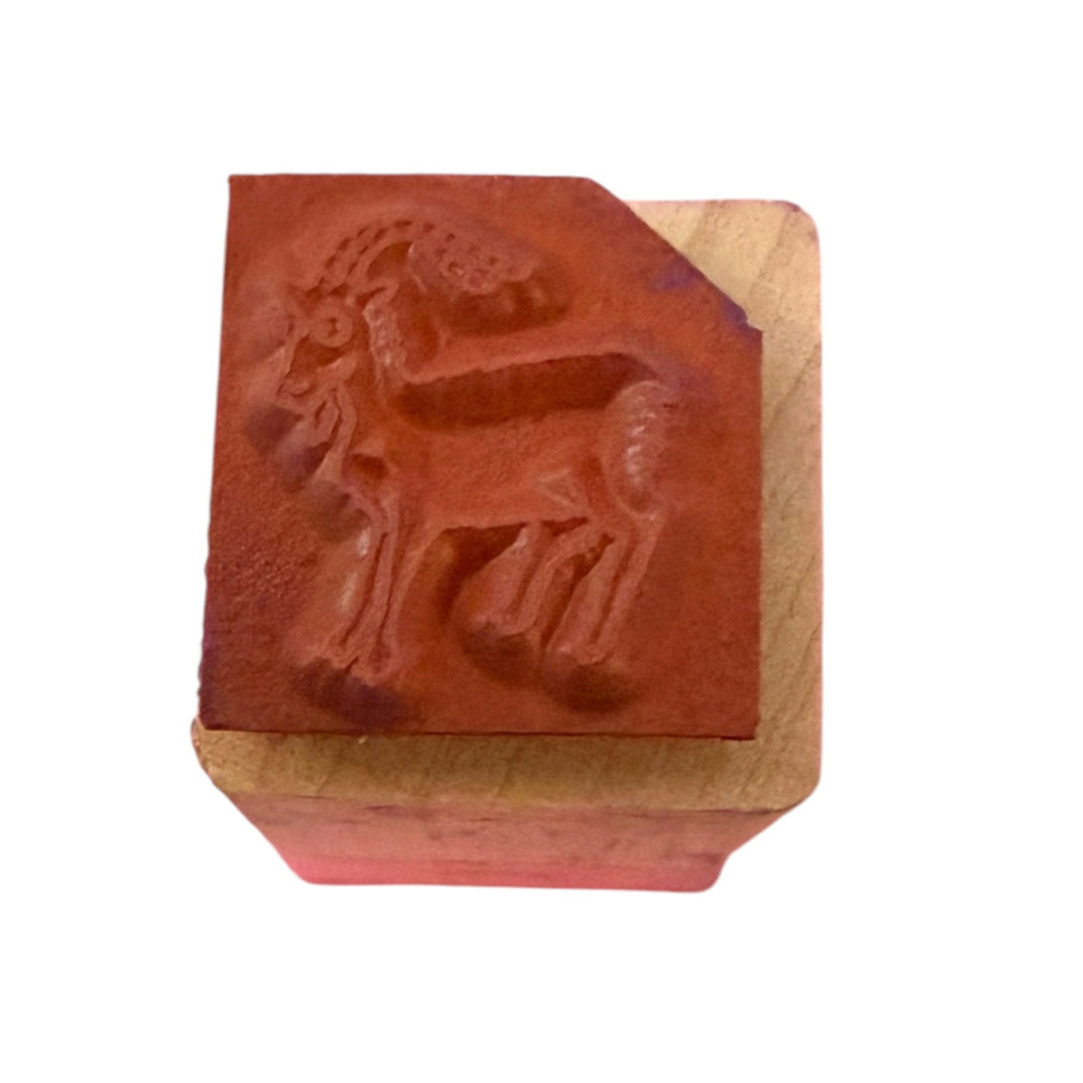 Red rubber stamp of a goat on a wood block with a white background