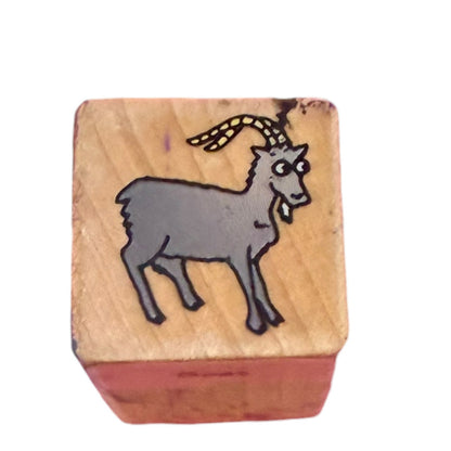 A wooden rubber stamp featuring a cartoon goat design on the top face, isolated on a white background.