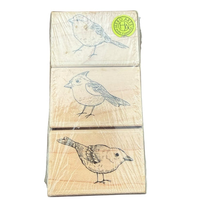 Three wooden stamp blocks stacked vertically, each printed with a different bird sketch in black ink, wrapped in clear plastic with a green circular logo sticker in the top right.