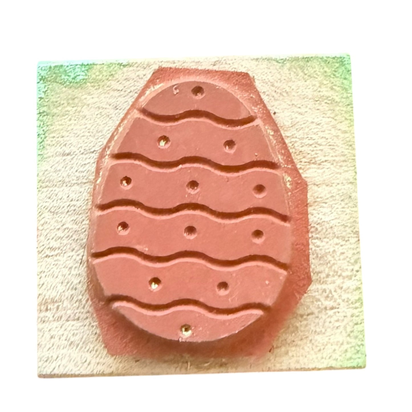 Rubber stamp with a wavy pattern and small dots, set against a textured beige background with a green painted corner.