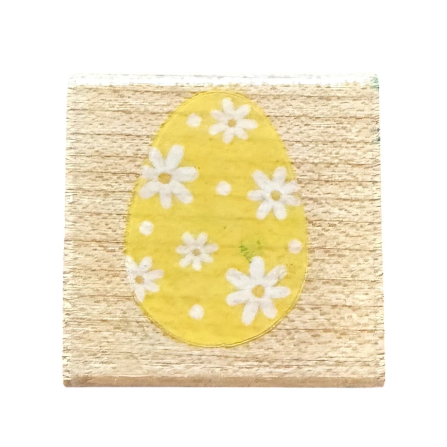 A square wooden block featuring a yellow egg design with white daisy flowers, set against a plain white background.