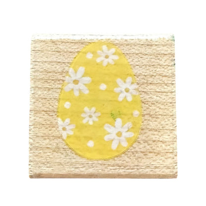 A square wooden block featuring a yellow egg design with white daisy flowers, set against a plain white background.