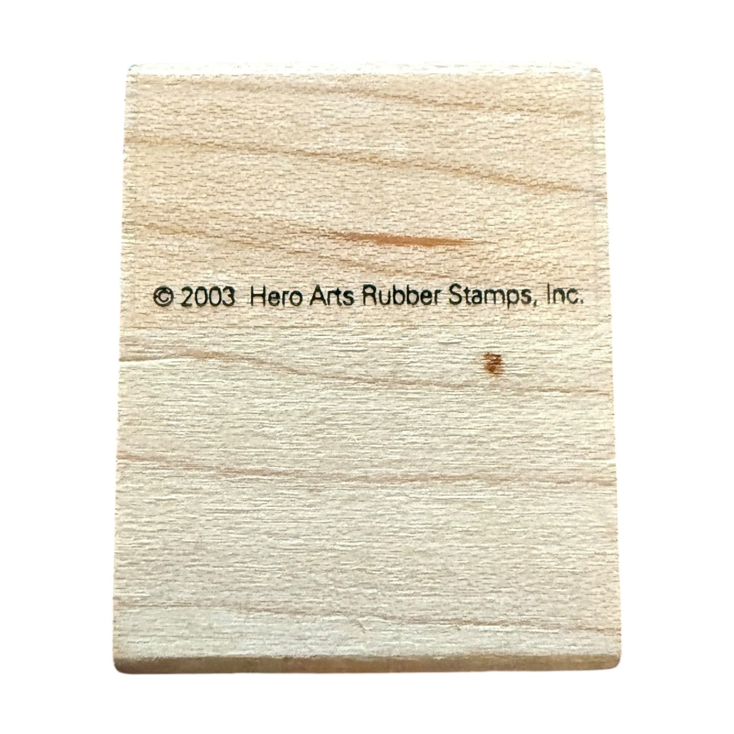 A square light beige wooden block with a black printed copyright notice reading '© 2003 Hero Arts Rubber Stamps, Inc.' in the center, isolated on a white background.