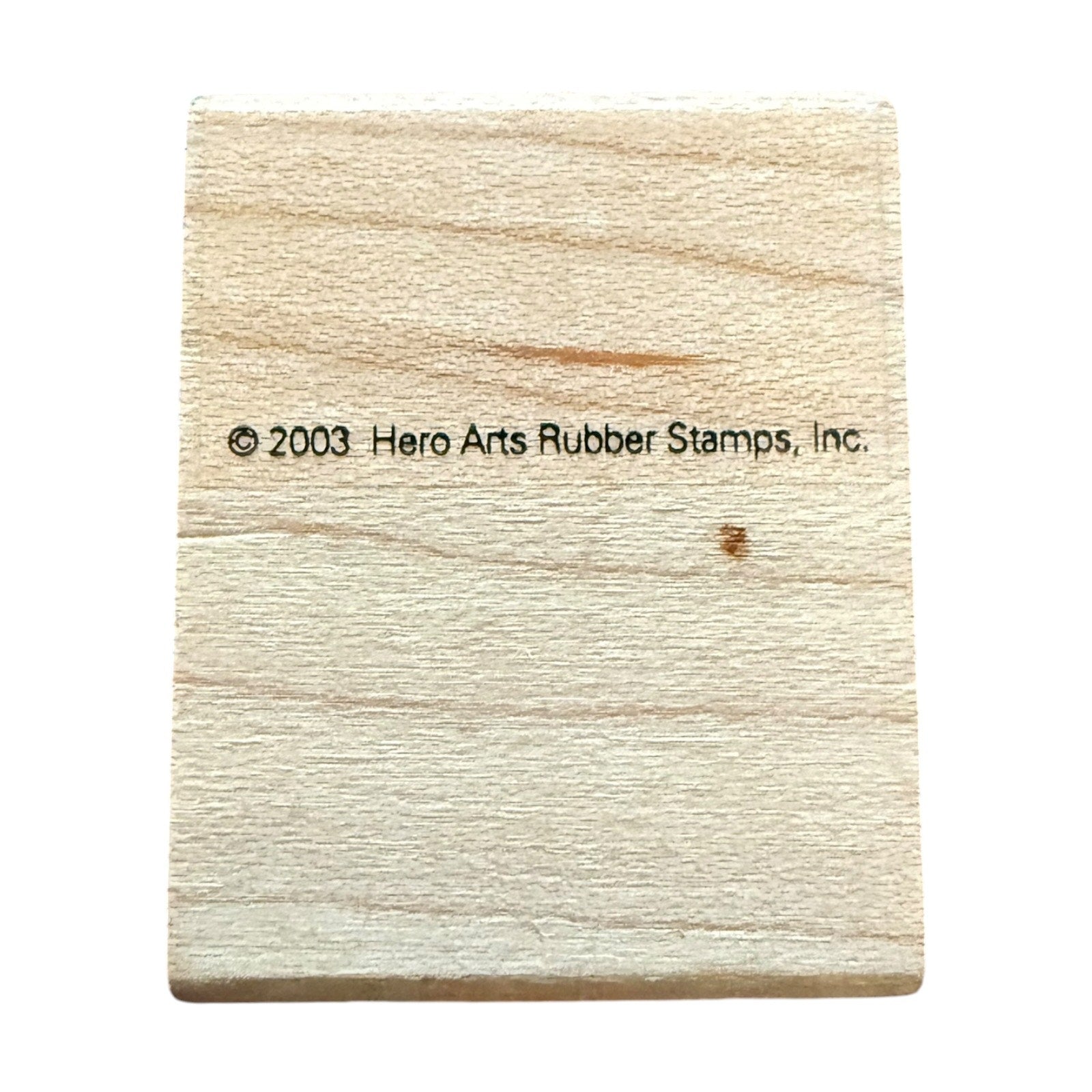 A square light beige wooden block with a black printed copyright notice reading '© 2003 Hero Arts Rubber Stamps, Inc.' in the center, isolated on a white background.