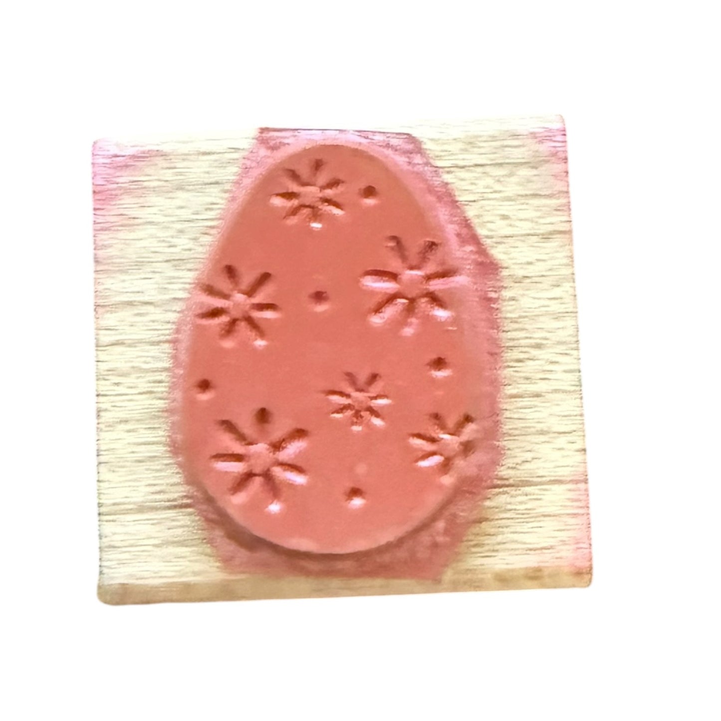 A pink rubber stamp with an Easter egg design featuring flowers and dot patterns, mounted on a light-colored wooden block.
