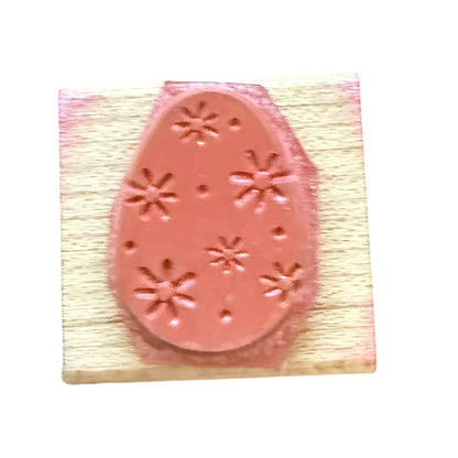 A pink rubber stamp with an Easter egg design featuring flowers and dot patterns, mounted on a light-colored wooden block.