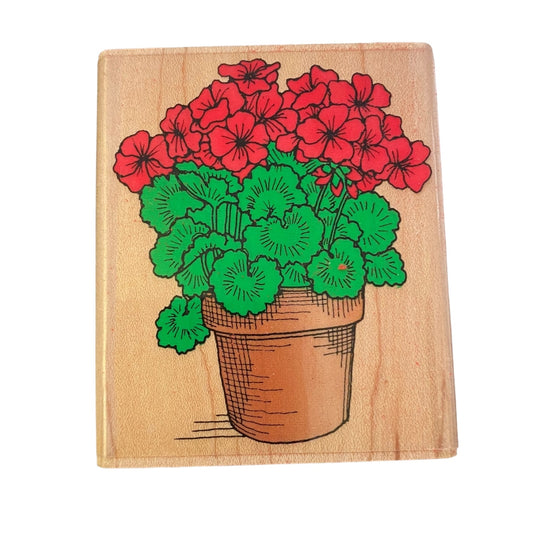 Wooden stamp with a design of red flowers and green leaves in a pot on a wooden block.