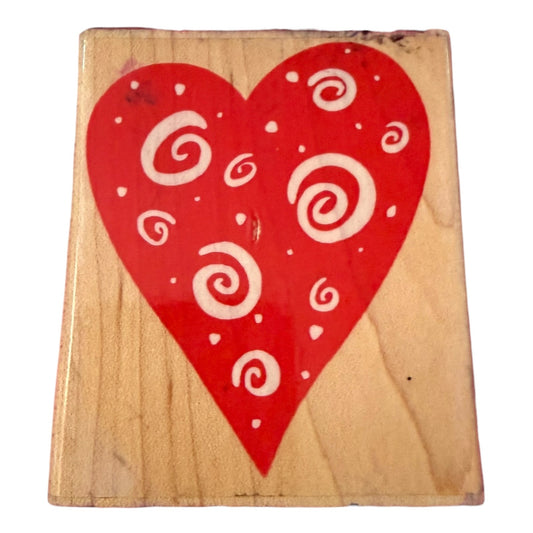 A square wooden stamp featuring a large red heart printed on the front, decorated with white swirl patterns and small white dots, shown against a plain white background.
