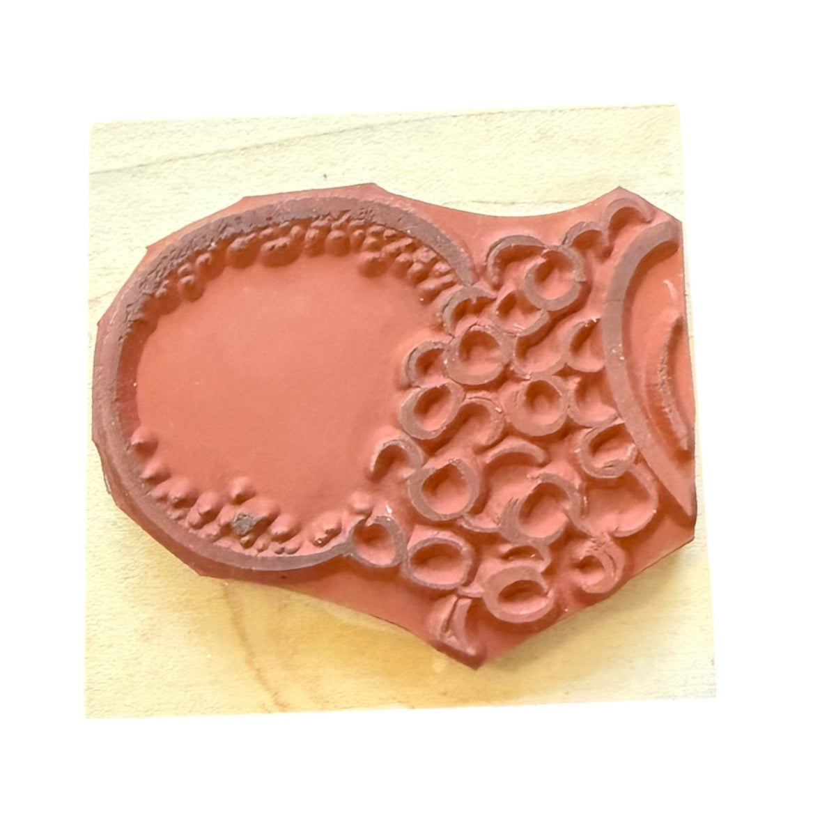 A terracotta-colored stamp , mounted on a square beige wooden block against a white background.