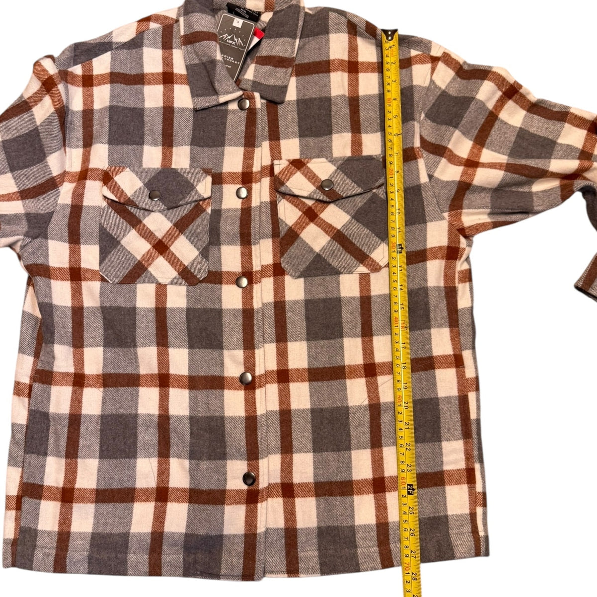 A long-sleeve plaid flannel, shown with a yellow tape measure running vertically along the side to indicate size.