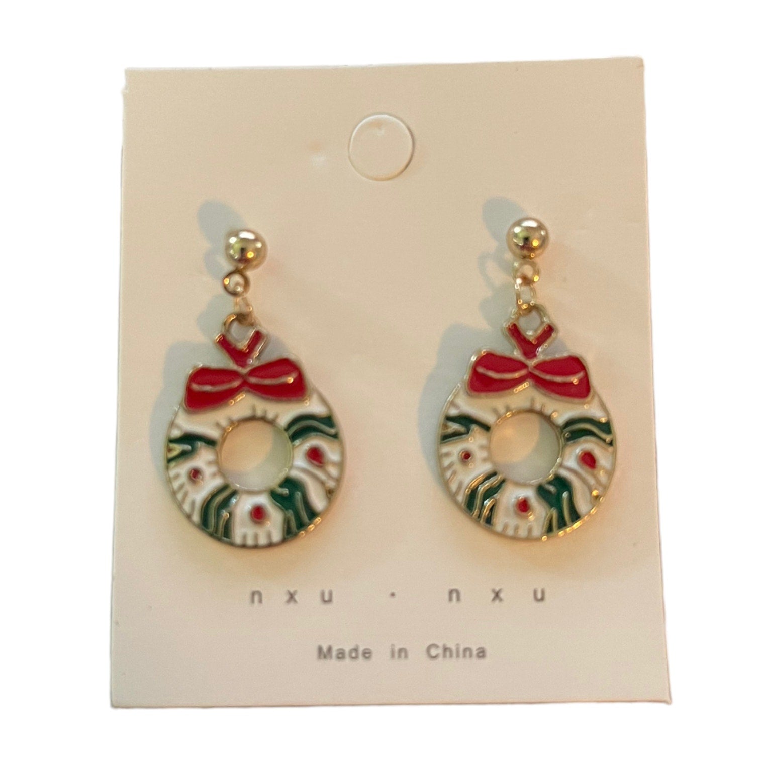 A pair of gold-tone dangle earrings shaped like wreaths, with red bows, green leafy details, and small red dots, displayed on a white card labeled 'nxu'.