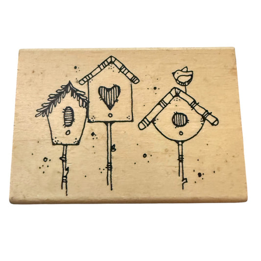 A rectangular wooden stamp with a black design of three birdhouses and small birds, shown on a plain white background.