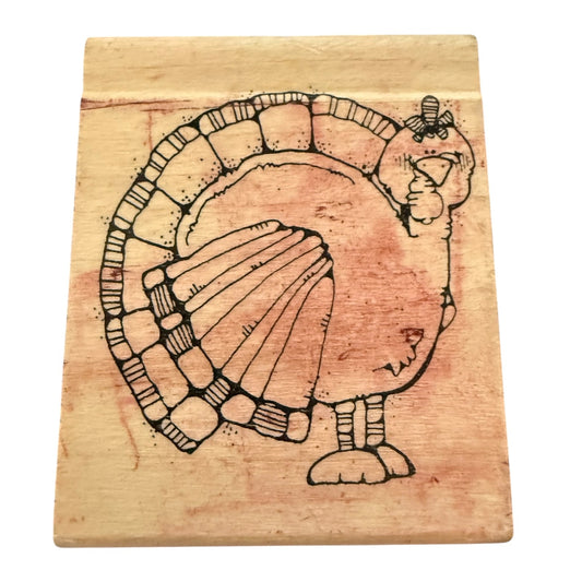 A stamp featuring a turkey design in black ink over a warm tan wood surface, shown against a plain white background.