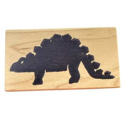 A rectangular wooden stamp with a black silhouette of a Stegosaurus dinosaur, shown on a plain white background.