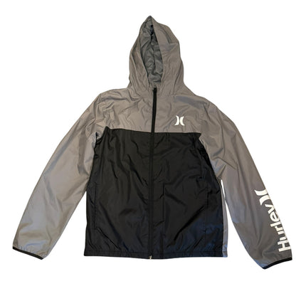 A colorblock hooded windbreaker jacket by Hurley, featuring a gray upper body and sleeves, a black lower body panel, a white logo on the left chest, and white script branding down the right sleeve, laid flat against a white background.