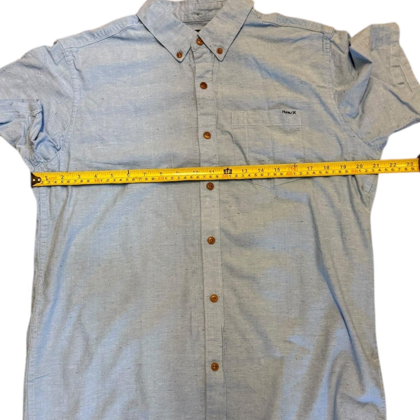 Light blue button-up shirt with a measuring tape on a white background