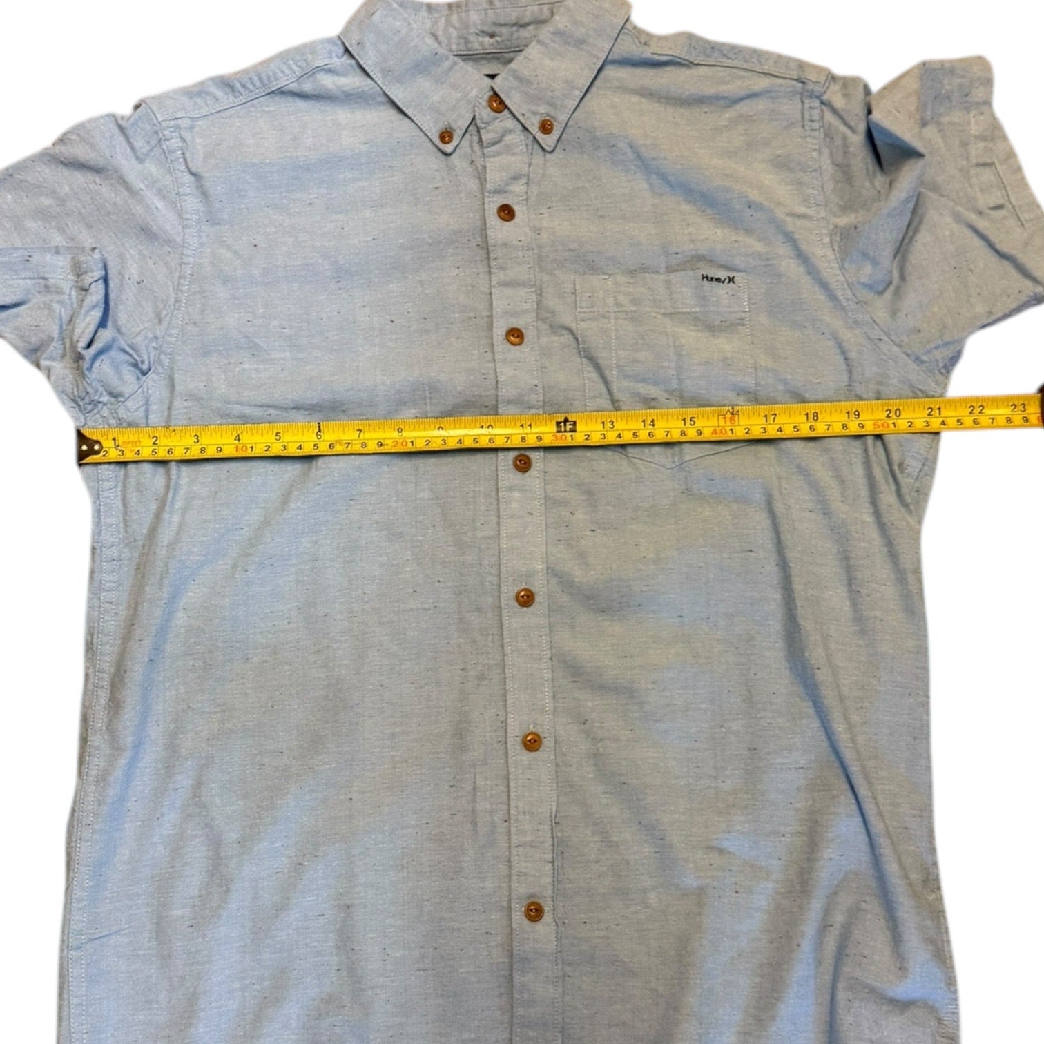 Light blue button-up shirt with a measuring tape on a white background
