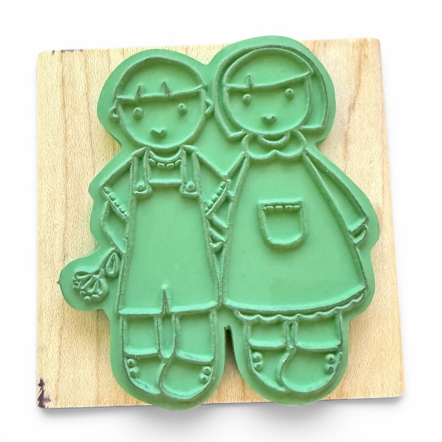 Green rubber stamp shaped like two children on a wooden board