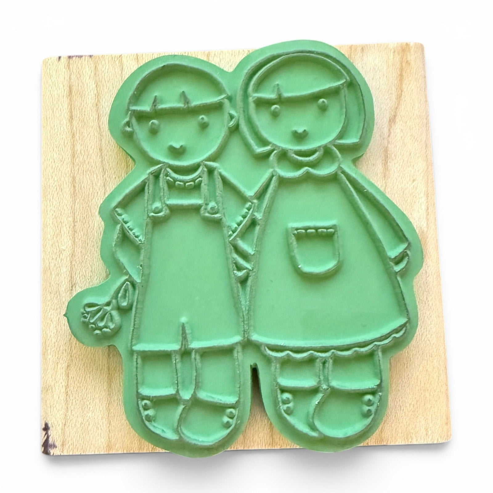 Green rubber stamp shaped like two children on a wooden board