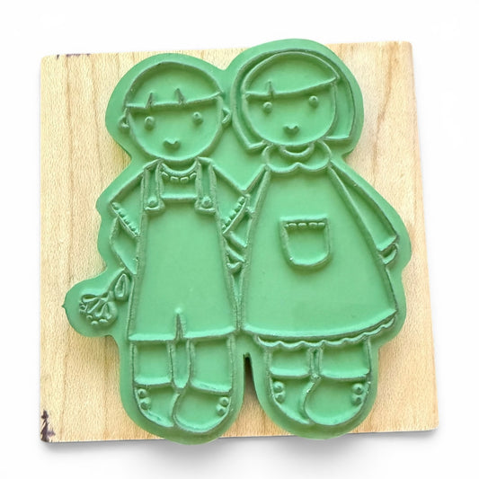 Green rubber stamp shaped like two children on a wooden board