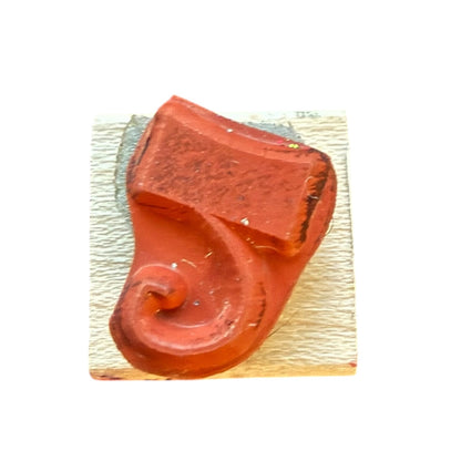 A red rubber stamp on a textured white paper square, isolated on a white background.
