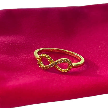 A gold infinity ring with textured pavé detailing, displayed on a vibrant magenta background.