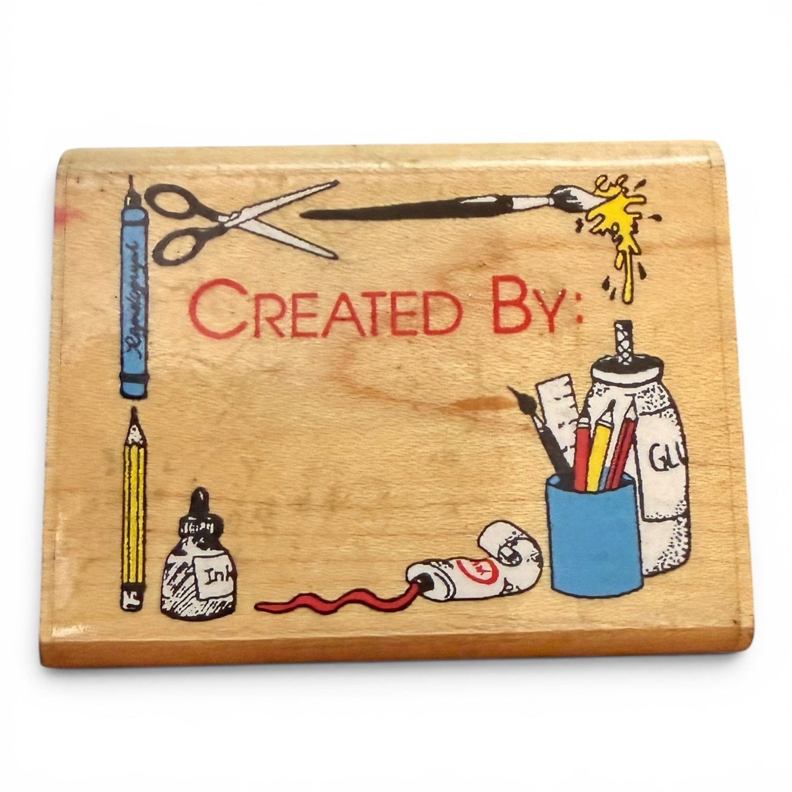 Wooden block with hand-drawn illustrations of stationery items and the text 'Created By'.