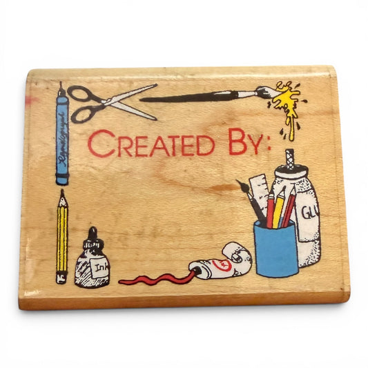 Wooden block with hand-drawn illustrations of stationery items and the text 'Created By'.