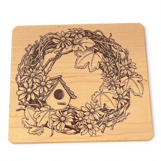 Wooden stamp with engraved design of a birdhouse, flowers, and leaves on a white background