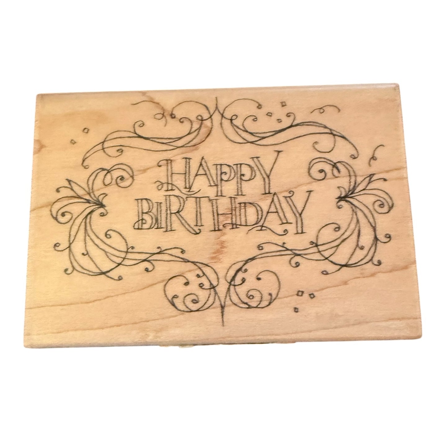 A rectangular wooden stamp featuring the words 'HAPPY BIRTHDAY' in decorative black scrollwork, shown on a plain white background.