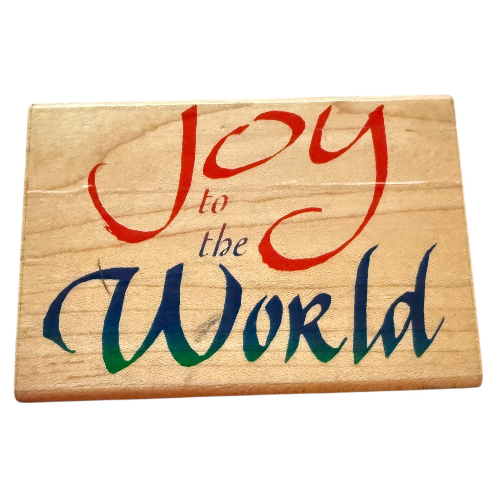 Wooden sign with 'Joy to the World' in red, blue, and green on a white background