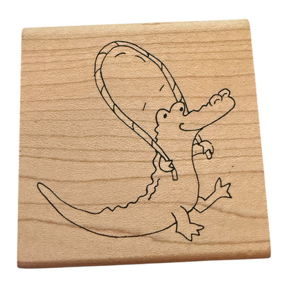 A square wooden block with a simple black line drawing of a cartoon alligator holding a jump rope, shown on a plain white background.