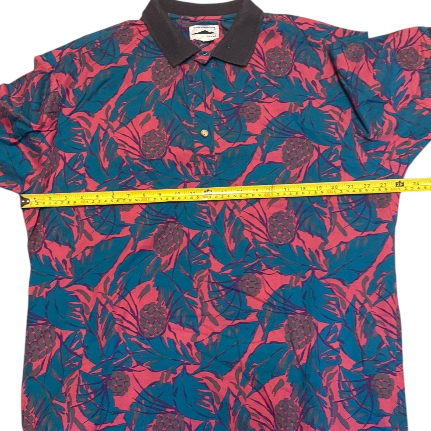 Short-sleeve shirt with a pink and blue leaf pattern, measured with a tape measure.