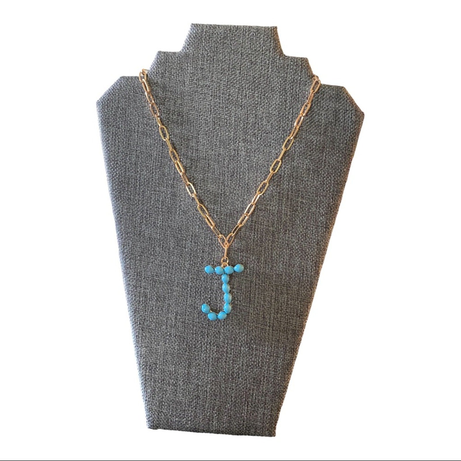 A gold chain necklace with a letter 'J' pendant made of small turquoise-blue beads, displayed on a gray fabric jewelry bust against a white background.