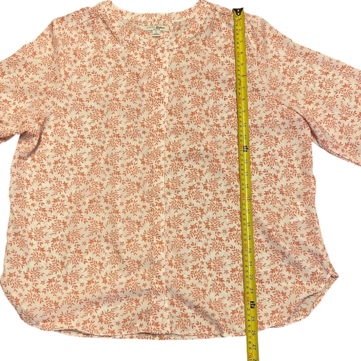 A women's blouse with a pink floral pattern on a white background, shown flat with a yellow measuring tape running vertically to indicate size.