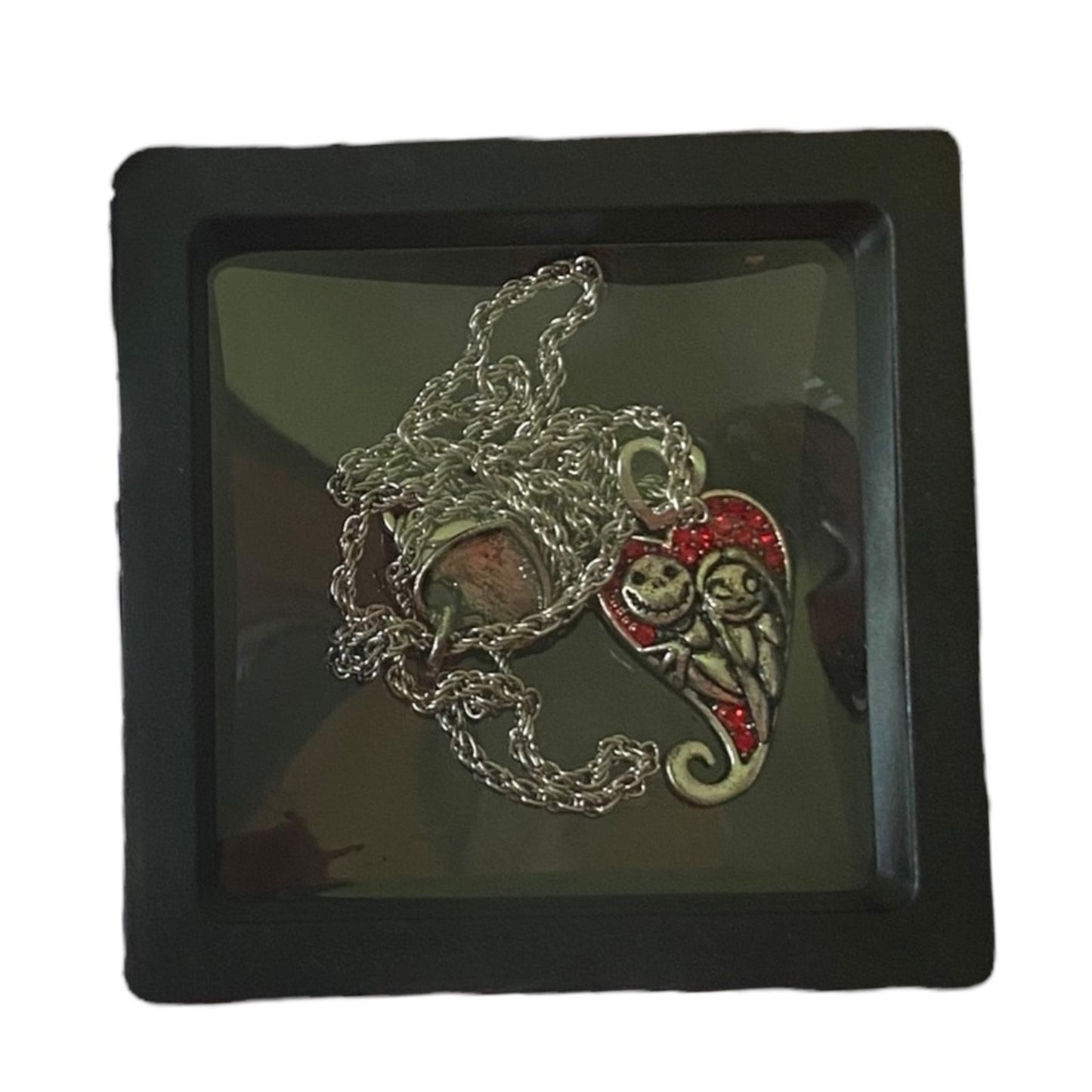 A necklace featuring silver-tone charms of Jack Skellington and Sally , displayed in a black box with a clear cover.
