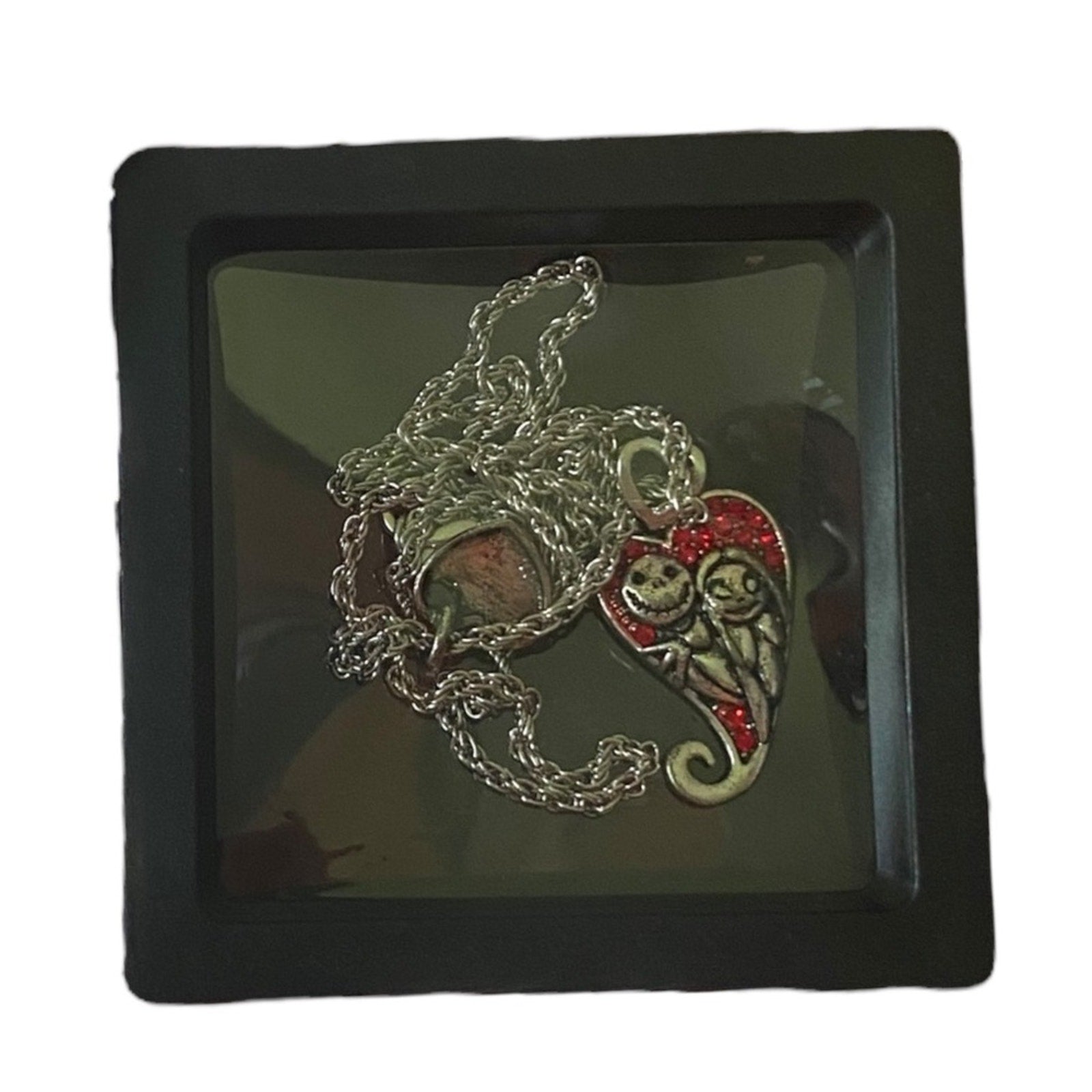 A necklace featuring silver-tone charms of Jack Skellington and Sally , displayed in a black box with a clear cover.