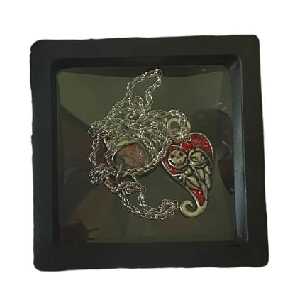 A necklace featuring silver-tone charms of Jack Skellington and Sally , displayed in a black box with a clear cover.