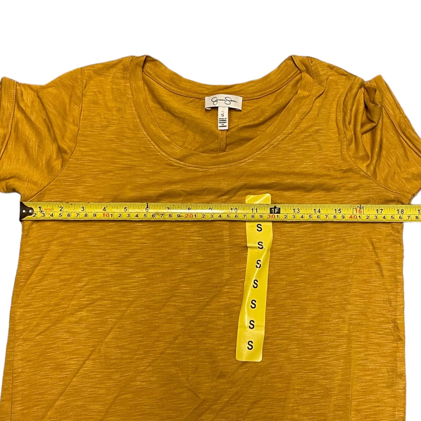A mustard yellow short-sleeve t-shirt dress laid flat on a white background, with a yellow measuring tape stretched across the chest to show the width and a size tag hanging from the tape.