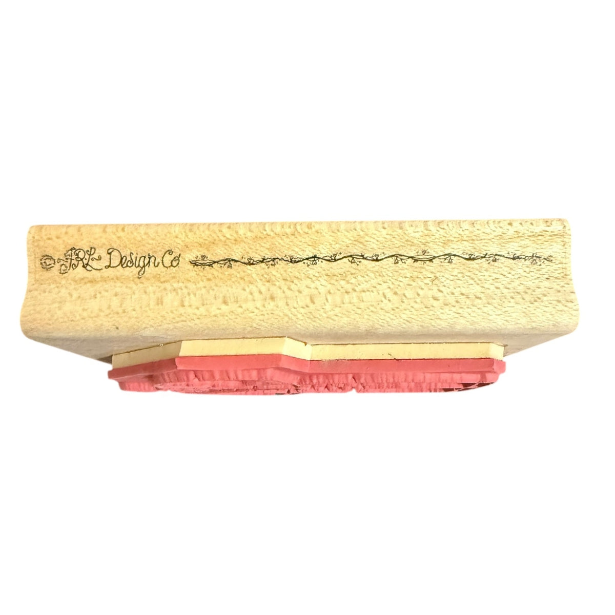 A close-up of a stamp block with a textured beige wooden top featuring the brand name 'JRL Design Co' in black script, supported by layered pink and beige rubber stamps, shown against a plain white background.