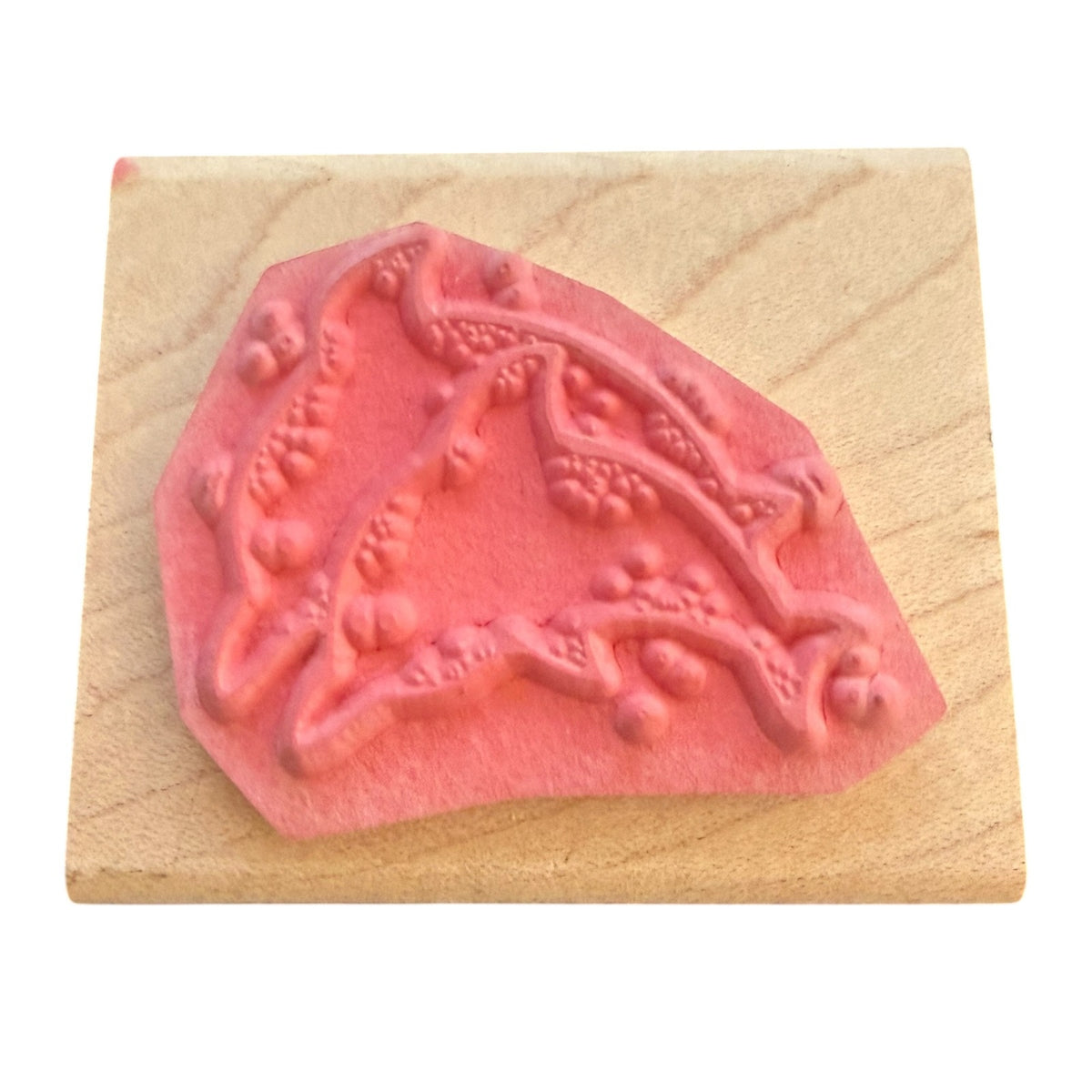 A pink rubber stamp with an embossed pattern, mounted on a square light wood block against a plain white background.