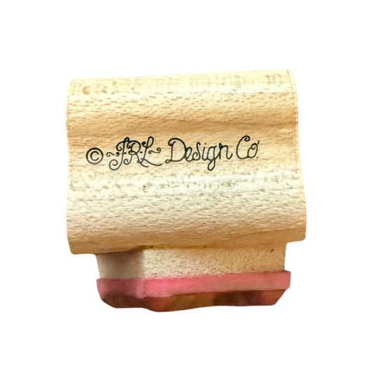 Wooden stamp with pink ink pad and 'JRL Design Co' branding on a white background