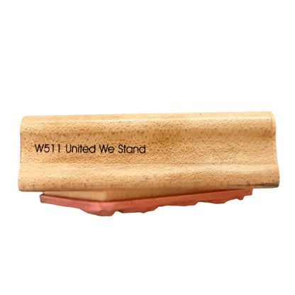 A wooden block stamp with the text 'W511 United We Stand' on a light wood surface, resting on a reddish-brown rubber base against a plain white background.