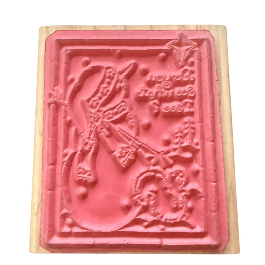 A pink rubber stamp with a detailed Christmas design mounted on a light-colored wooden block.