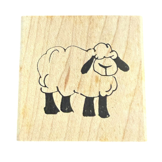 A square wooden stamp block featuring a simple black line drawing of a sheep on a light natural wood background, isolated on a white backdrop.