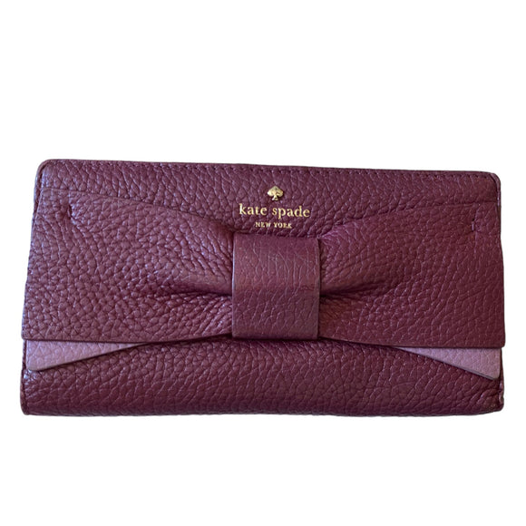 Purple wallet with a bow and 'kate spade New York' logo on a white background