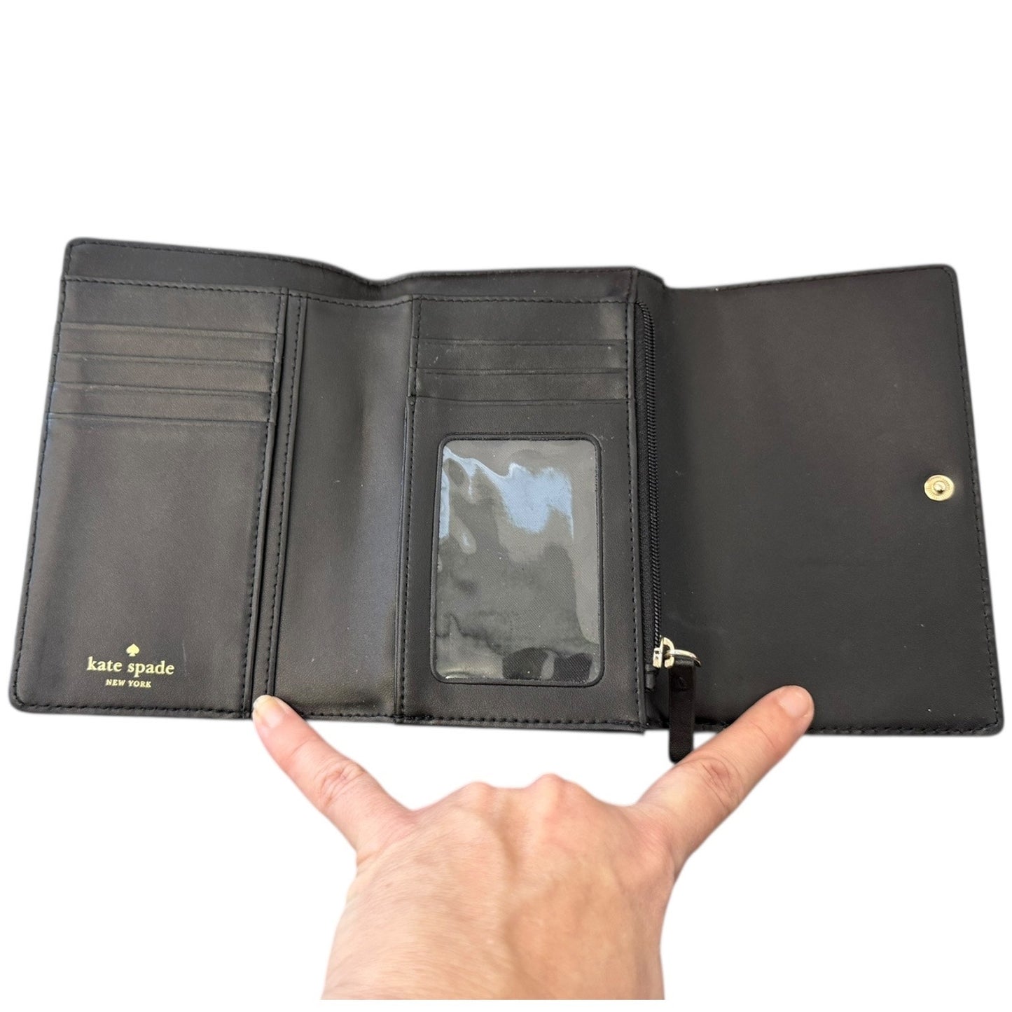 Black wallet with 'kate spade New York' branding held open by a hand on a white background