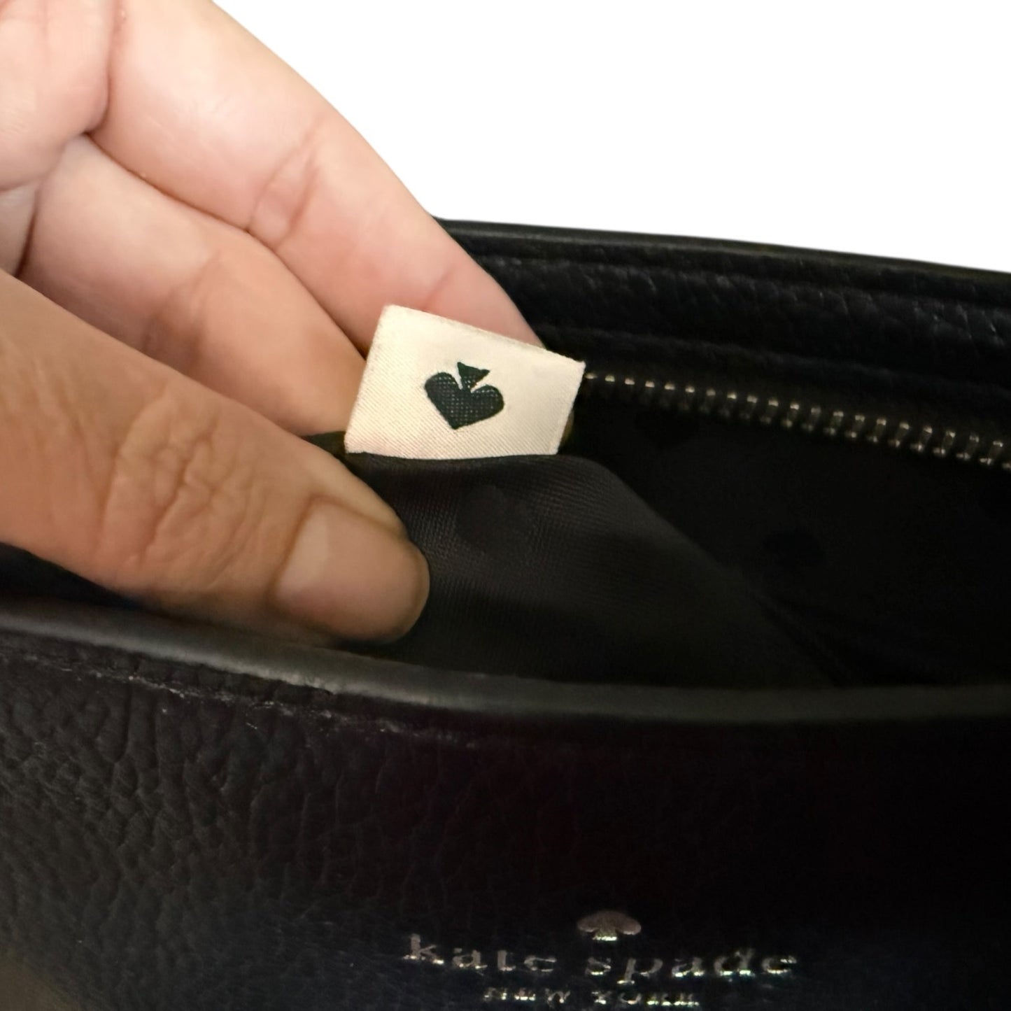 Hand holding a black Kate Spade purse with a visible brand label.